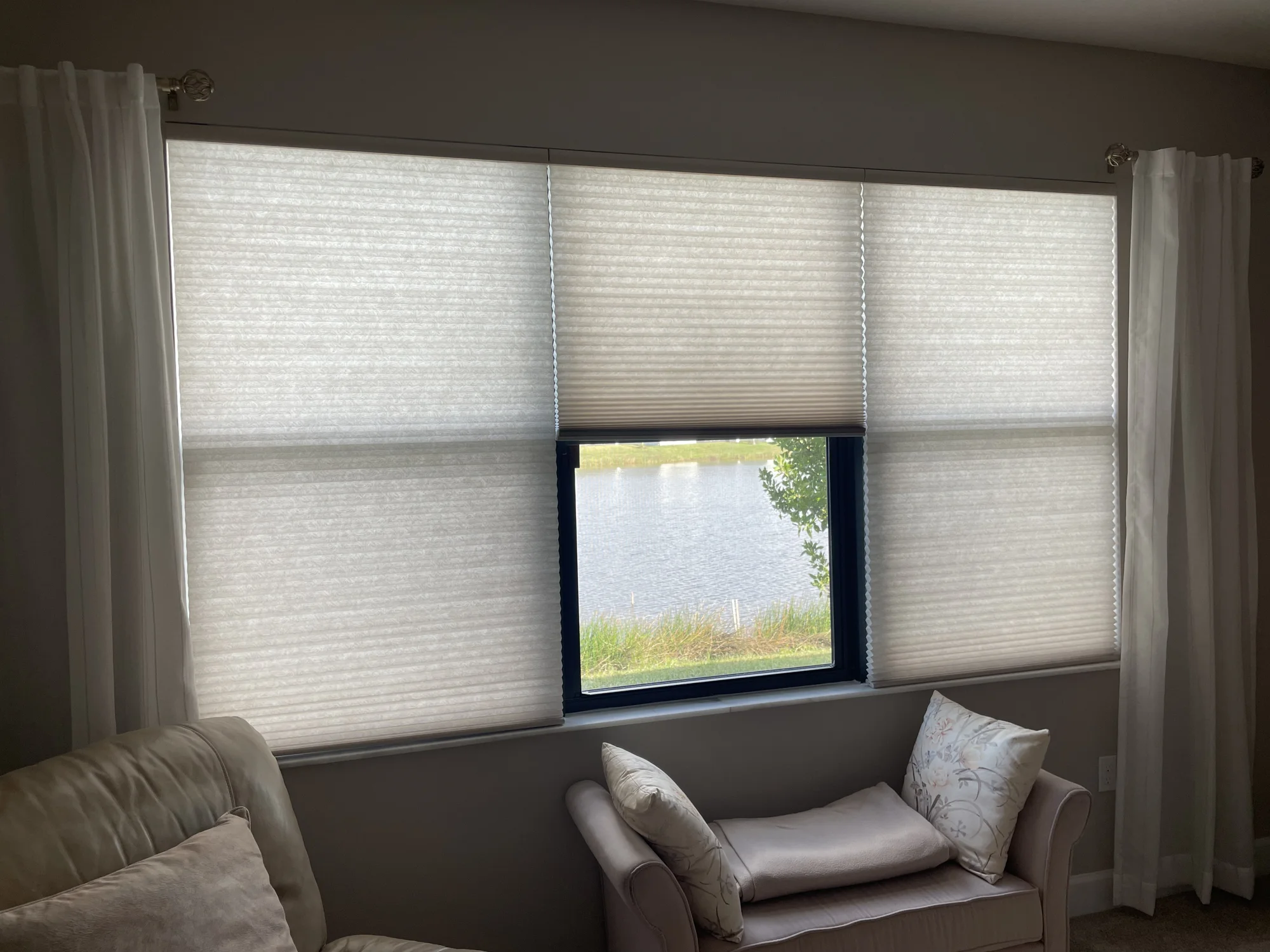Cellular honeycomb shades over a triple window with a lake view