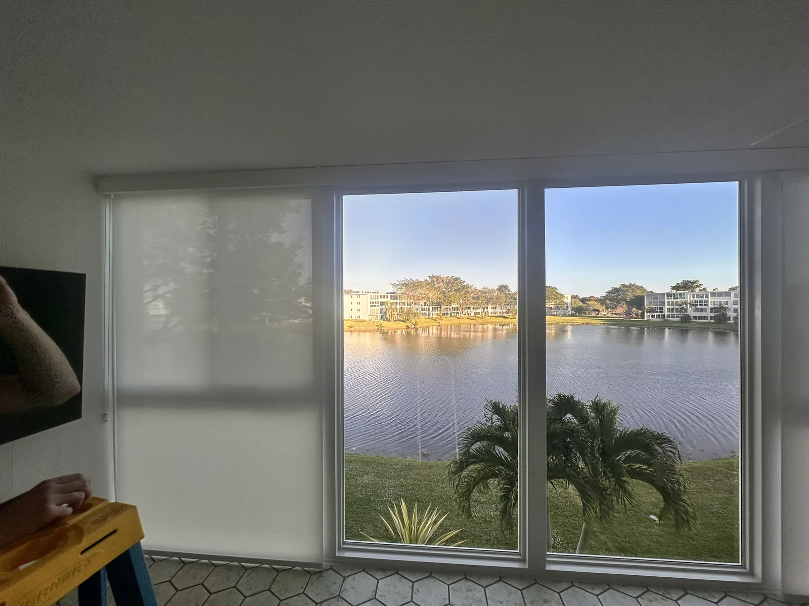 Roller shades across a wall of windows overlooking a lake