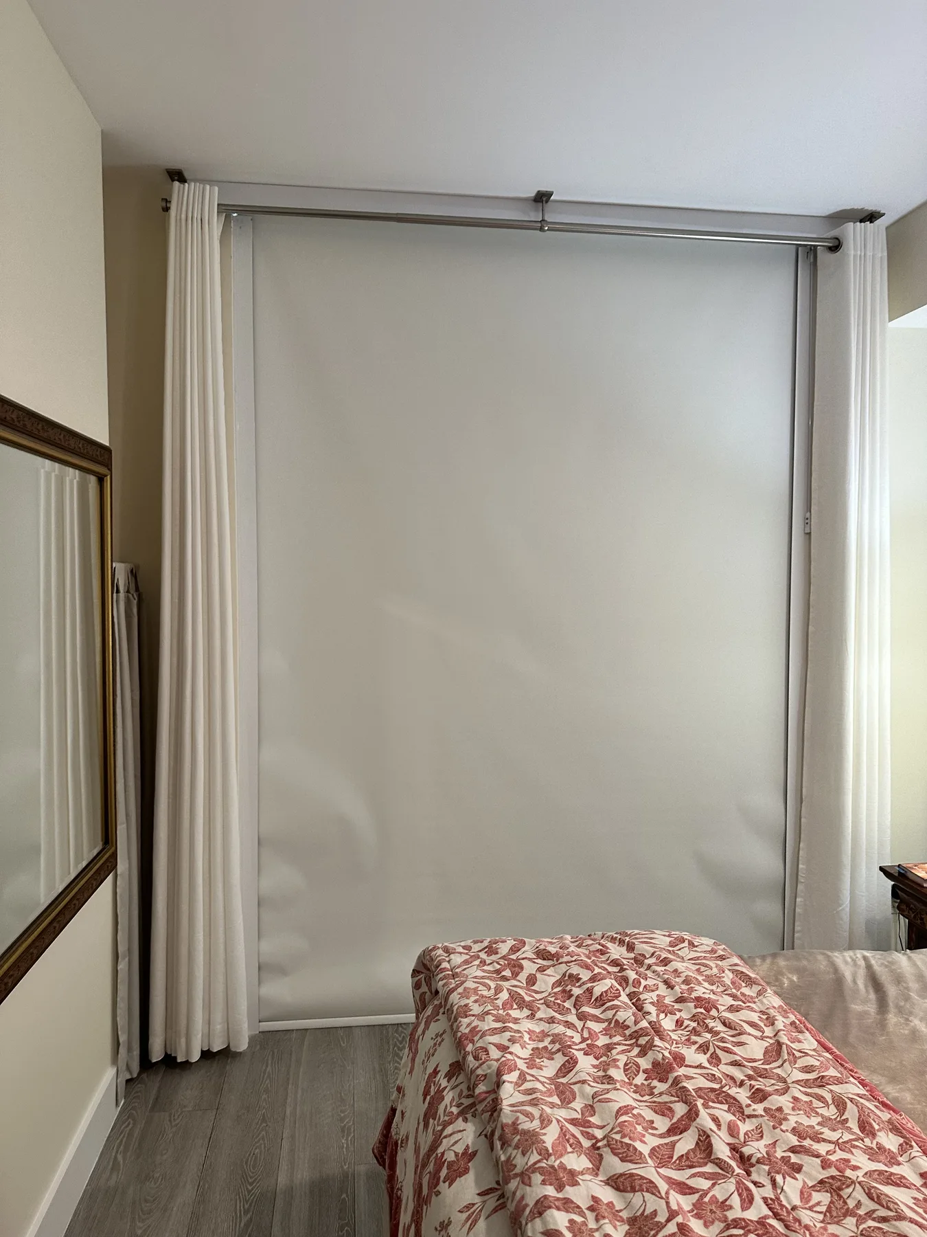 Blackout roller shade in a bedroom, side channel sealing the edge behind floor-length drapery